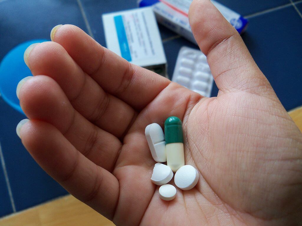 Image of multiple different shaped pills in the palm of a hand